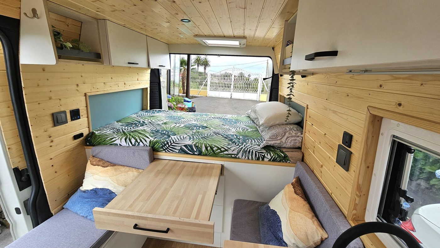 Interior de una camper de Murcia Camper con cama, mesa de madera y sofás
